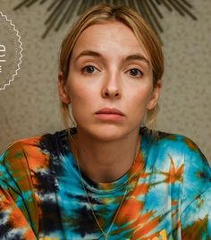 a woman wearing a tie - dyed shirt is staring at the camera