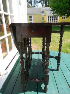 an old wooden table sitting on top of a green deck next to a yellow house