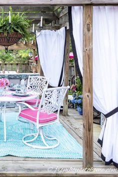 an outdoor dining area with white chairs and pink cushions on a blue rug under a pergolan