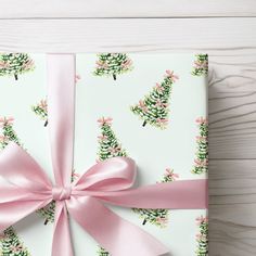 a present wrapped in pink ribbon and decorated with christmas trees on white wood planks