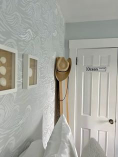 a hat hanging on the wall next to a bed with white sheets and pillows in front of a door