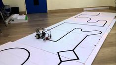 a robot is sitting on the floor in front of a large piece of paper that has been cut out