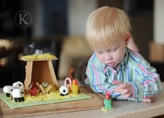 a little boy sitting at a table playing with toy farm animals and building his house