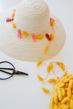 a straw hat, scissors and thread on a white table with yellow flowers around it