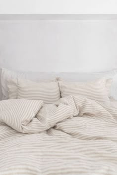 an unmade bed with white linens and striped sheets on it, in a bedroom