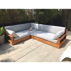 a wooden couch sitting on top of a cement floor next to a potted plant