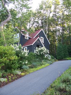 a black house surrounded by trees and bushes on a road in front of the house