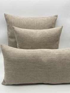 two beige pillows sitting next to each other on top of a white surface with one pillow in the middle