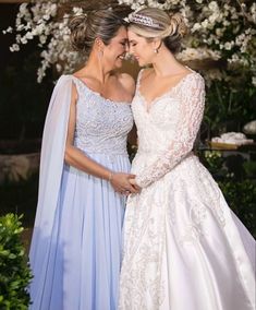 two women dressed in wedding gowns standing next to each other and smiling at each other