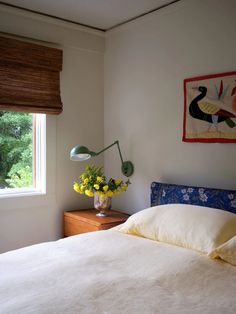 a bed with white sheets and yellow flowers on the headboard next to a window