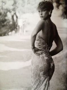 an old photo of a woman in a dress posing for the camera with her hands on her hips