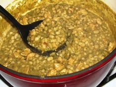 a red pot filled with food on top of a stove next to a black spoon