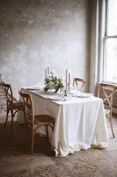 the table is set for two with candles and flowers on it in front of an open window