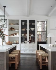 an open kitchen with white cabinets and wooden stools in the center, filled with dishes