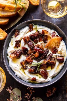 a bowl filled with whipped cream and dried fruit on top of a wooden table next to bread