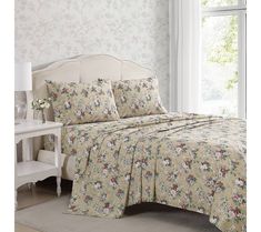 a bed in a bedroom next to a window with white curtains and a floral print on it