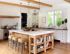 a kitchen with an island and several stools next to the counter top in front of two windows