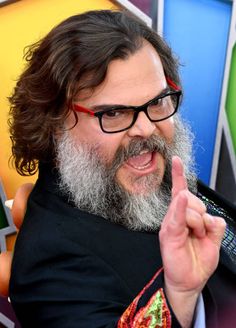 a man with long hair and glasses making the middle finger sign while standing in front of a colorful background