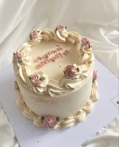 a birthday cake with white frosting and pink flowers on it's top is sitting on a piece of paper