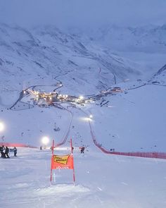 a ski slope covered in snow at night with people walking on it and lights shining