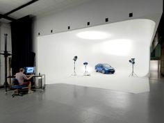 a man sitting in front of a blue car on top of a white wall next to microphones