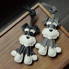 two dog key chains are sitting on a wooden table, one is black and the other is white