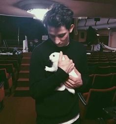 a man holding a small white dog in his arms while standing next to an auditorium