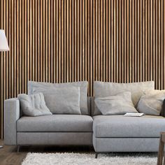 a grey couch sitting on top of a white rug next to a lamp and wooden wall