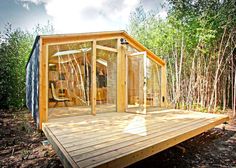 a wooden deck in the woods with a glass door on it's side and trees around