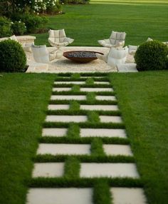 a stone path in the middle of a grassy area with white chairs and a fire pit