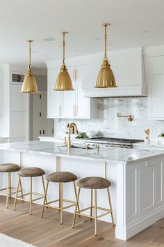 a kitchen with white cabinets and gold pendant lights hanging from the ceiling over the island