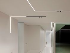 an empty hallway with white walls and flooring is lit by recessed light fixtures