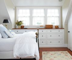 a white bed sitting in a bedroom next to a dresser and window with two windows