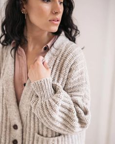 a woman is wearing a sweater and holding her hand on her shoulder while looking off to the side