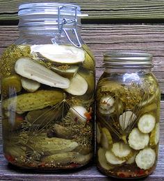 two jars filled with pickles sitting on top of a wooden table