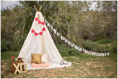 a teepee with hearts on it is sitting in the grass next to some pillows