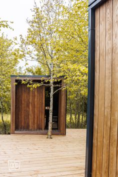 a small wooden structure sitting on top of a wooden floor next to a tree in the woods