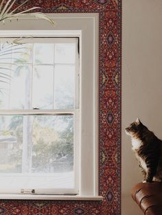 a cat sitting on top of a leather chair next to a window with a palm tree in the background