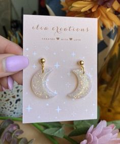 a pair of earrings that are sitting on a card next to flowers and a vase