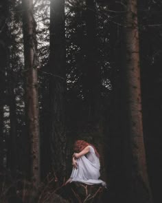 a woman with red hair is sitting in the middle of some trees and has her arms around her head