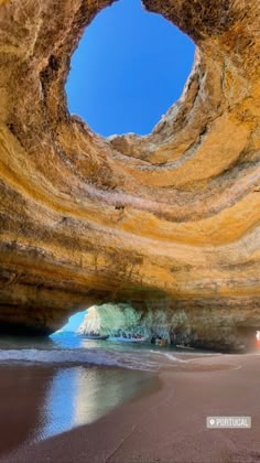 the inside of a cave with water and sand on the beach below it is a blue sky