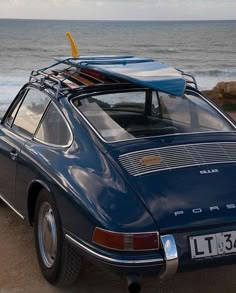 an old blue porsche with a surfboard on the roof is parked by the beach