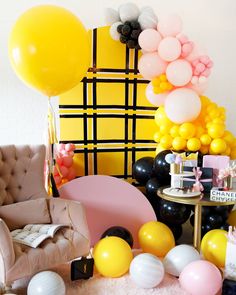 a room filled with balloons and furniture next to a wall covered in black, white, and yellow balloons