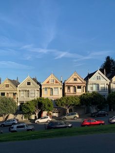 a row of houses with cars parked on the street in front of them and trees