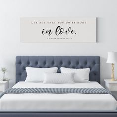 a bed with white pillows and a blue headboard in a room that has a quote on the wall above it