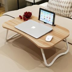 a table with a laptop, tablet and mouse on it in front of a bed