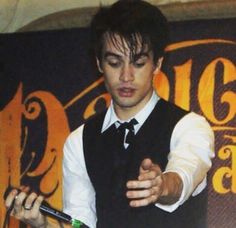 a man in a vest and tie holding a cell phone while standing next to a sign