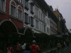 many people are walking down the street in front of tall buildings with windows and balconies