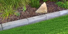 a rock sitting in the middle of a flower bed next to green grass and shrubbery