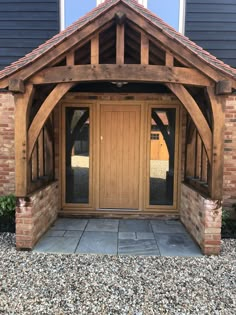 the front entrance to a home with wooden doors and brick pillars, surrounded by gravel